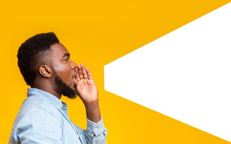 African american man making loud announcement at copy space, holding hand near his open mouth over yellow background, side view
