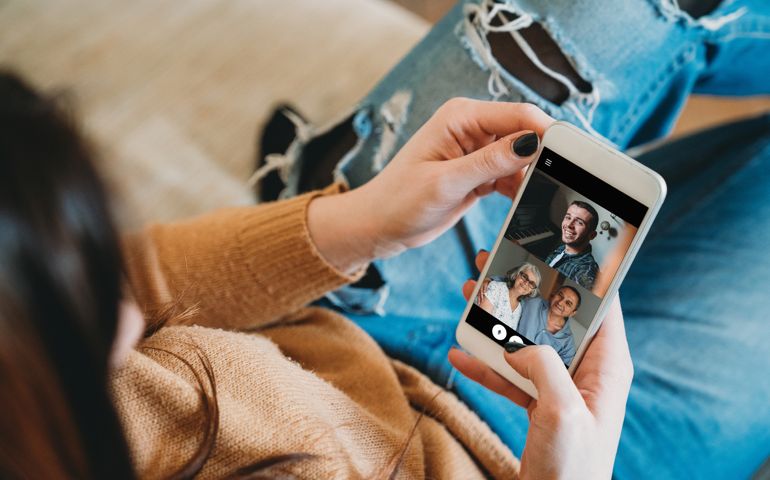 Young woman connecting with her family during quarantine. She's using a smartphone to call her family in Coronavirus COVID-19 time.