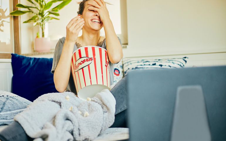 Cute woman eat popcorn and watching movie at home.