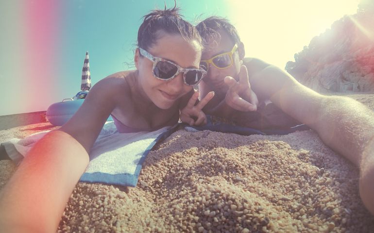 Portrait Of A Happy Young Couple Lying At Beach Gesturing Peace Sign. Light leeks added for vintage effect