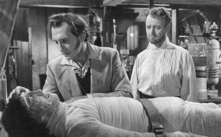 1957: Baron Frankenstein, played by Peter Cushing (1913 - 1994), leans over the monster he has created, Christopher Lee, as Robert Urquhart (1921 - 1995) looks on. The scene is from 'The Curse of Frankenstein', directed by Terence Fisher.