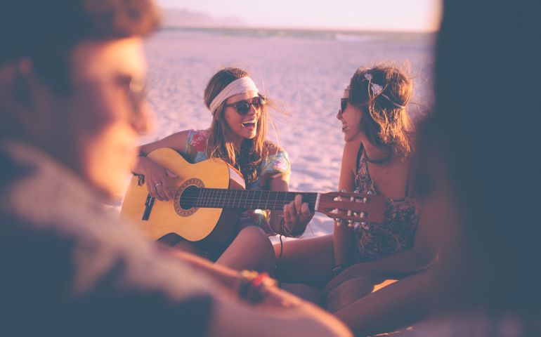 Girl playing guitar and singing for her friends at a summer evening beachparty