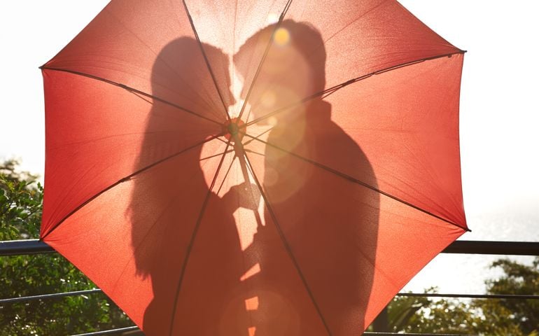 Silhouette of an affectionate couple standing behind an umbrella