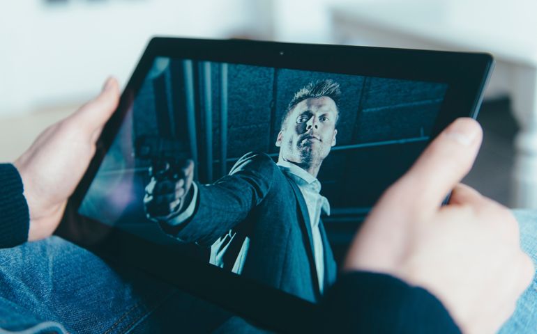 Concept of streaming a movie on digital tablet. Image on the screen of a bad guy holding a gun.