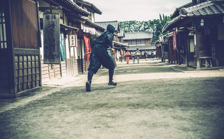 Ninja in black is chasing women in kimono and traders, peasants on the streets of an old city, Edo period, Kyoto, Japan, Asia. Ninja is runing away from the camera, in front of him honest people unaware of the danger.