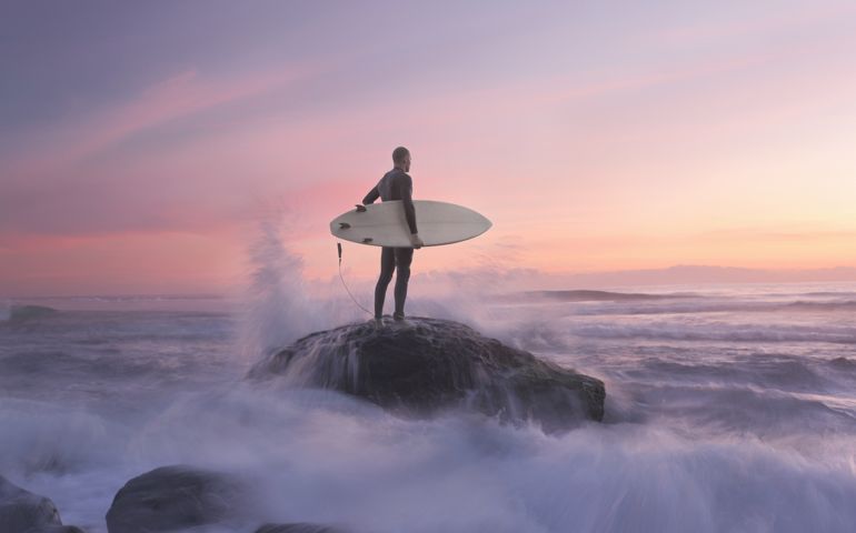 Surfer on rock against sunset, water around