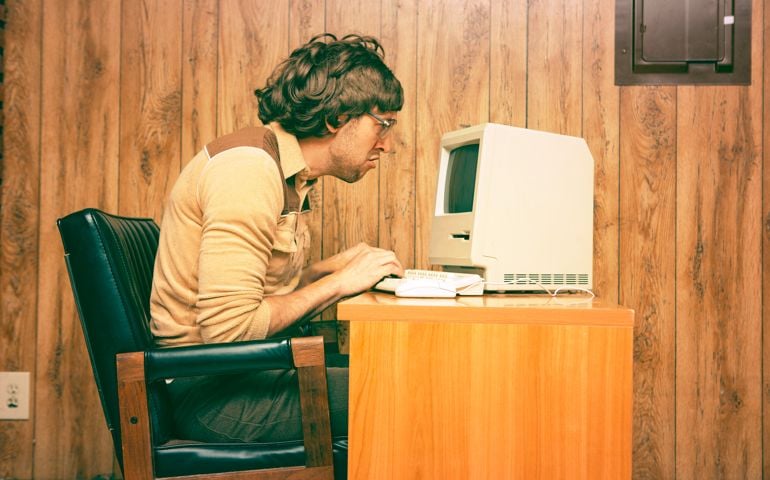 Goofy 1980s Computer Worker looking intently at a vintage computer screen. Retro colored and styled image with wood panelling in the background.