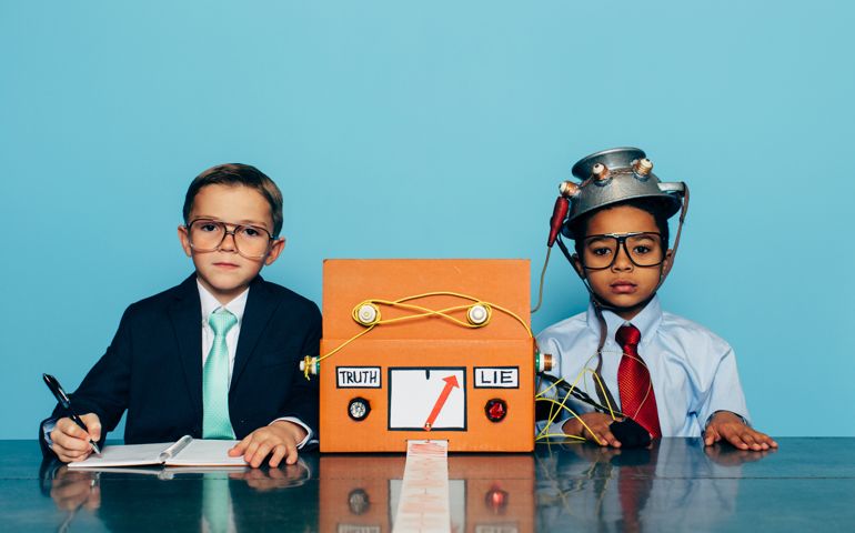 Two young boys and businessmen dressed in suits and glasses sit at a desk with a homemade lie detector machine. This serious interview is conducted in an office and the machine is predicting a lie from the job candidate. Dishonesty will eventually catch up to you.