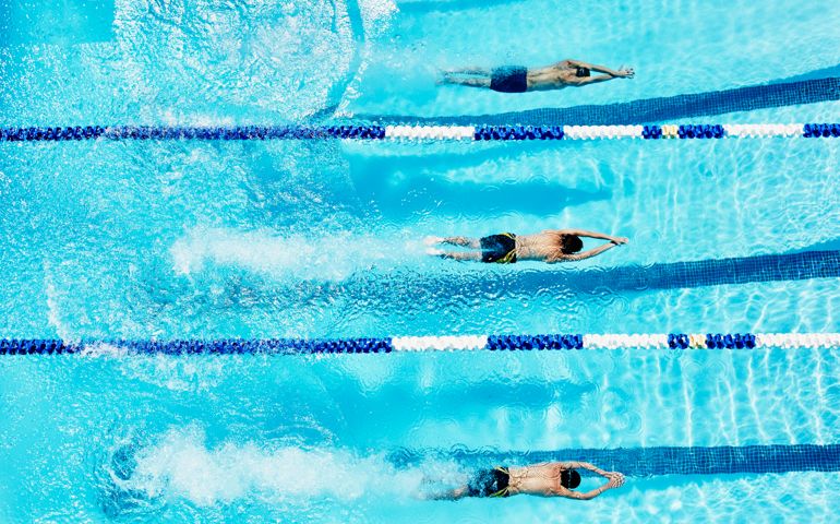 Competitive swimmers gliding underwater after diving into outdoor pool at start of race overhead view