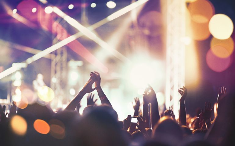 Closeup rear view of large group of people enjoying an open air concert on a summer night. There are a lot of hands raised.