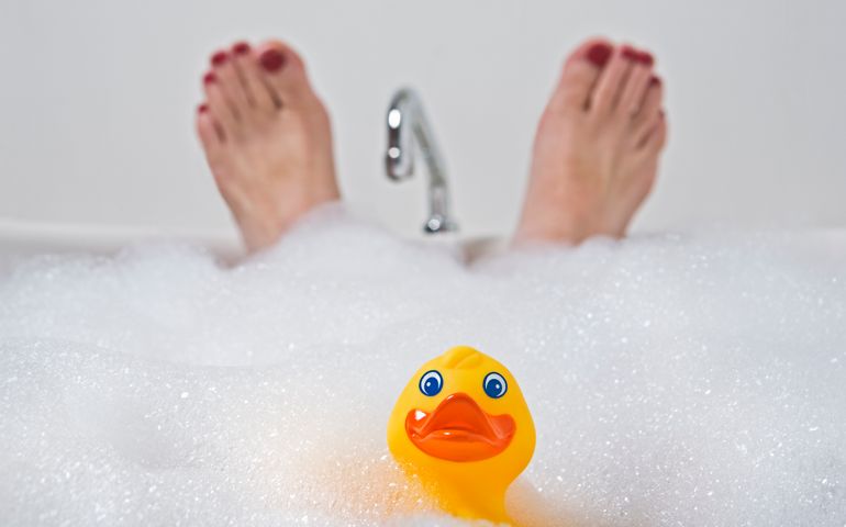 Toy duck and feet with painted toe nails in bubble bath.