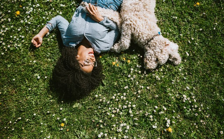 A happy young adult woman enjoys time at a park with her standard poodle, running, playing, and relaxing with the dog.