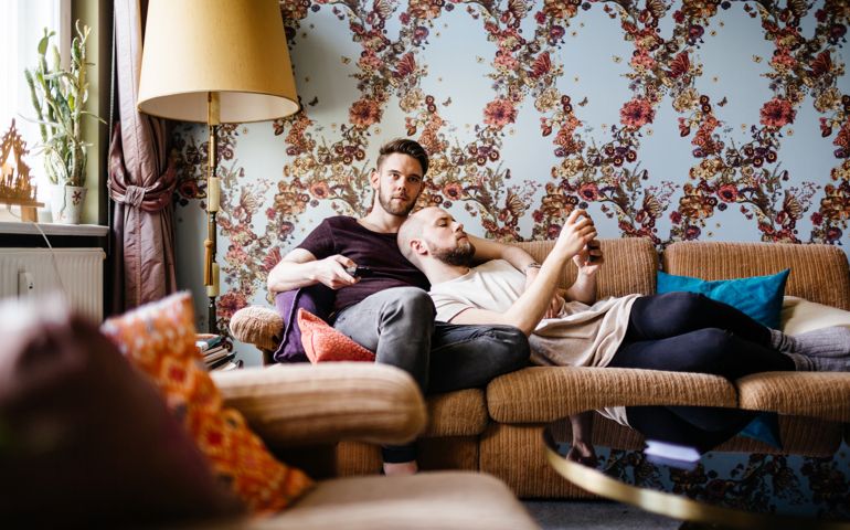 A gay couple relaxing while watching tv at home with each other.