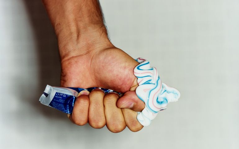 Man squeezing tube of toothpaste, close-up of hand