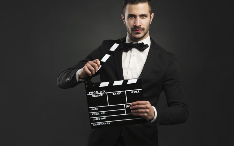 Portrait of a beautiful latin man with tuxedo and holding a clapboard
