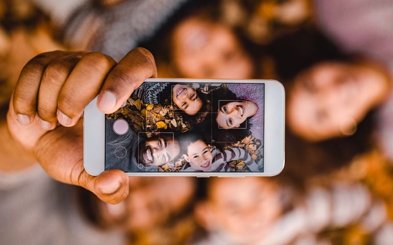 Close up of happy African American family having fun while taking a selfie with mobile phone while relaxing in autumn leaves.