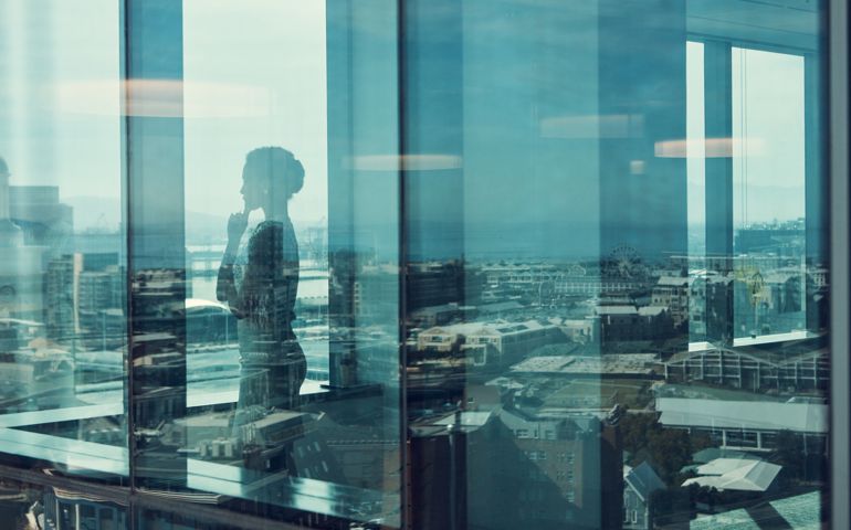 Shot of a businesswoman standing inside a glass building with a reflection of the city in the background