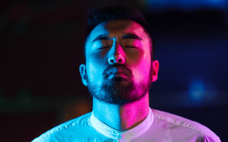 A portrait of a young man lit by a pink and blue neon light in the city.