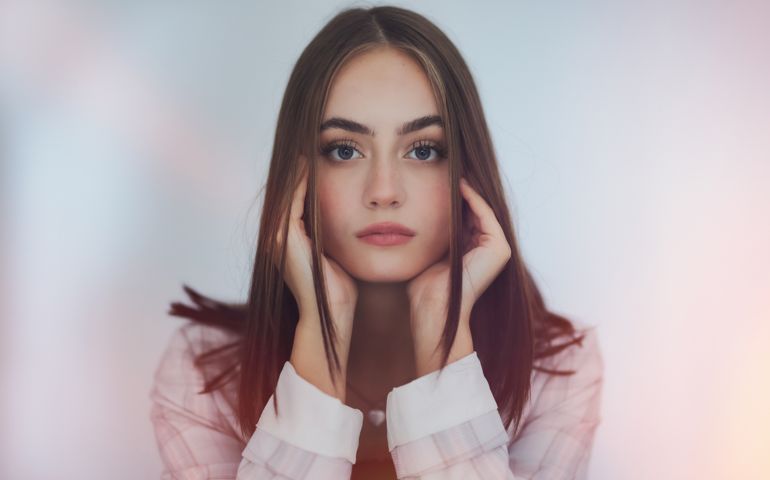 Attractive young woman looking straight into the camera, head on her arms. Millennial Generation Portrait. Edited Colors and blured light effect.