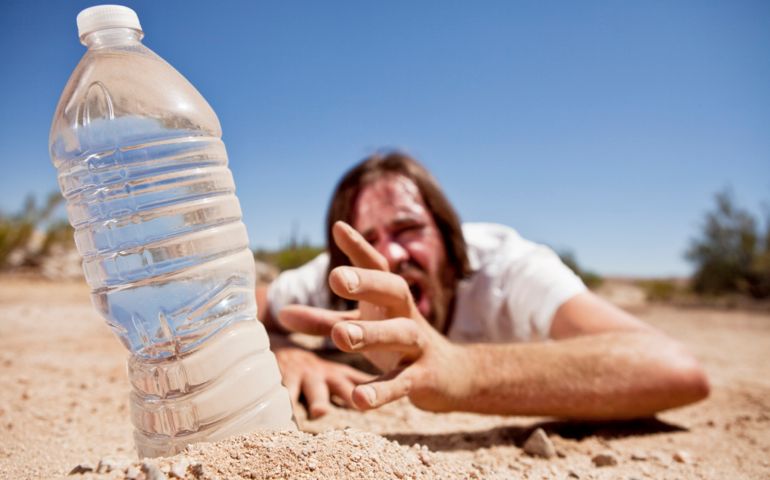 Dehydrated man crawling through the desert reaching for bottle of water.
