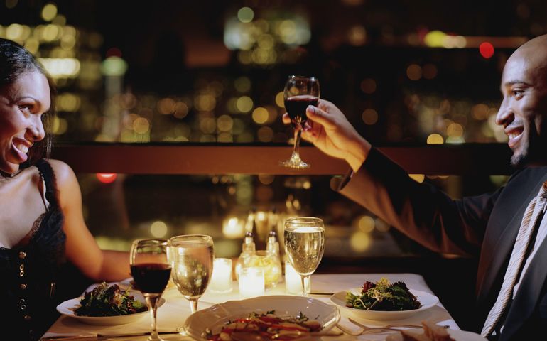Man toasting woman at restaurant table, side view