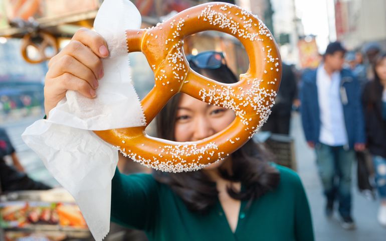Young attractive Asian girl holding a pretzel up to the camera, she purchased from street vendor food cart in NYC.