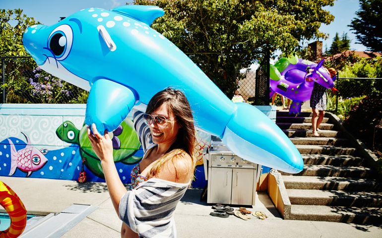 Smiling woman carrying large inflatable pool toy during backyard pool party