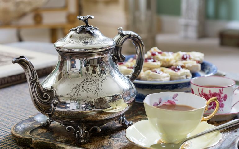 Silver teapot on tray with cups and saucers and scones
