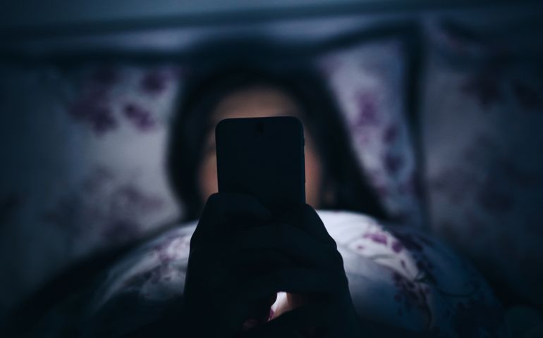 Woman texting and reading on smartphone in bed in midnight.