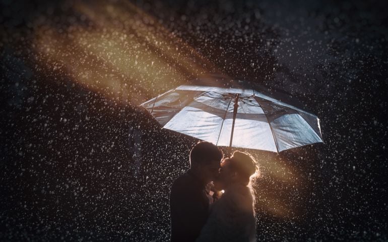 A couple kisses in the rain under an umbrella