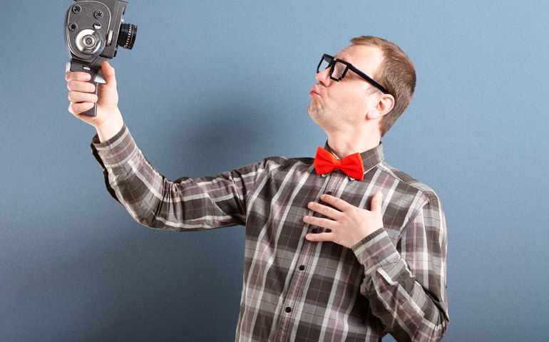 Handsome nerd guy wearing glasses sending kisses to old video camera and filming. behind him is blue background
