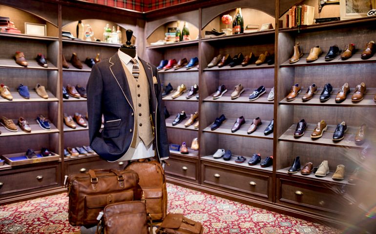 Interior of a high-quality shop for men with shoes on display. A cosy luxurious atmosphere. A mannequin on display wearing a blazer, waistcoat, shirt and tie. leather man bags also on show.