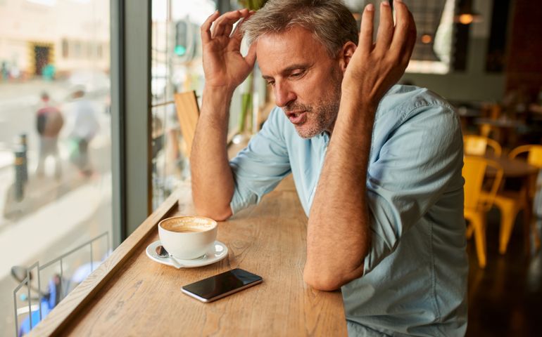Shot of a mature man looking stressed out while using his mobile phone at a cafe