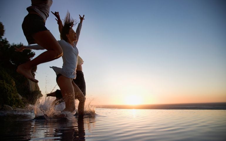 Friends jumping into infinity pool at sunset