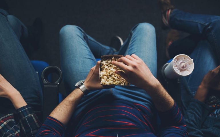 Unrecognizable young man watching the movie and eating popcorn in the cinema