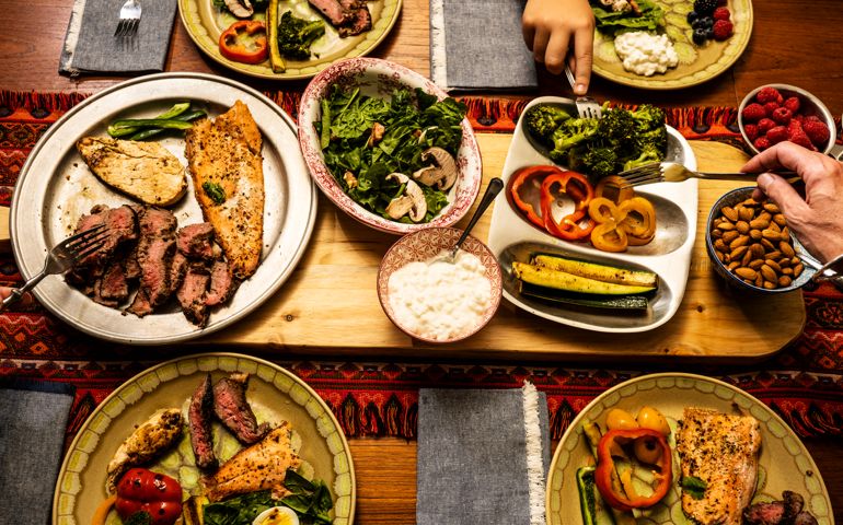 A ketogenic meal laid out on a dining table with the hands of people serving themselves. A keto diet is a low carb, high fat diet that avoids many fruits.