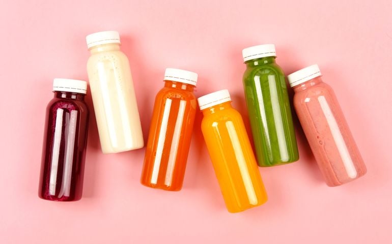 Bottles of multicolored smoothies or juices on pink background