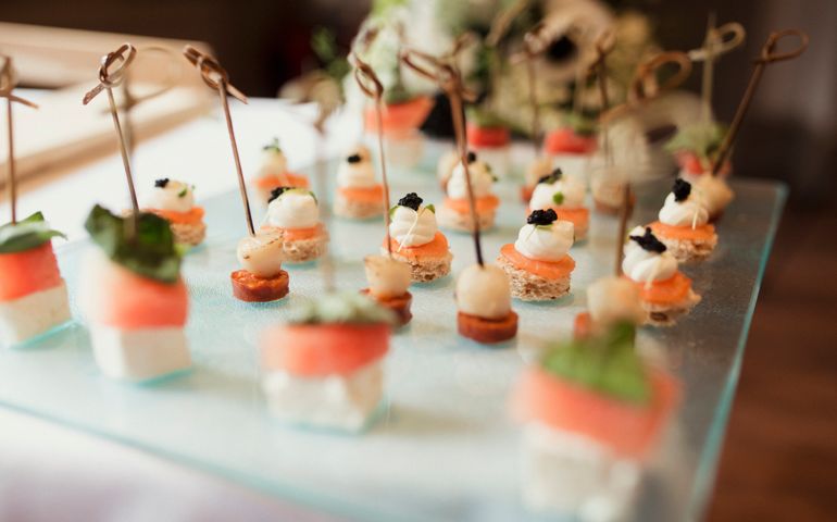 Close up of small salmon based canapés ready to eat being served on a glass platter.