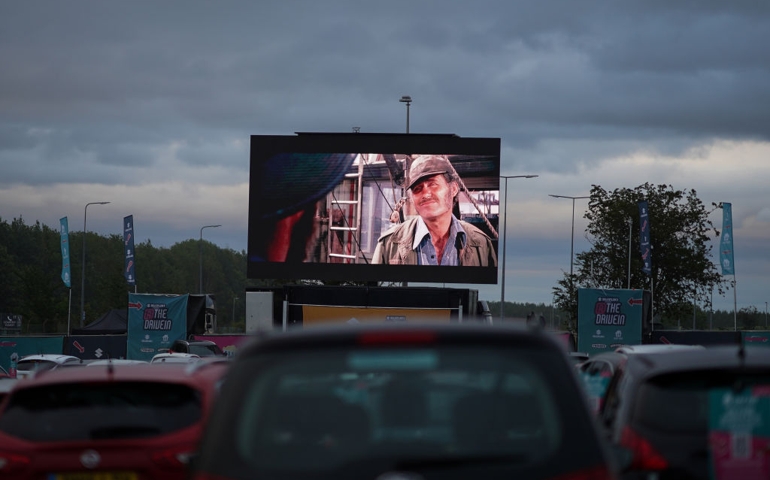Cars park up to watch a showing of Jaws during a drive-in cinema experience at Newcastle Airport on August 05, 2020 in Newcastle upon Tyne, England. The venue at Newcastle airport is one of 12 venues around the country that will host the drive-in cinema tour offering 80’s classics and 2010’s blockbuster movies. Entertainment is provided ahead of each screening with stand-up comedy, bingo and ‘careoke’. Due to coronavirus restrictions cars are parked 2-metres apart during the screenings and other safety measures have been put in place. Food can be ordered by those attending using a special app and which is then delivered to the cars by staff. A number of tickets at each of the screenings will also be offered for free to NHS and care workers who wish to attend.