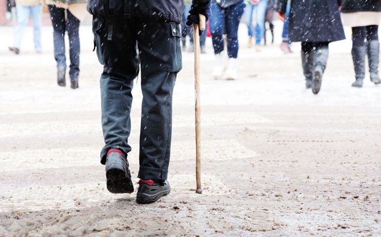 Wet and snowy zebra crossing. Man with cane walking with cane support.