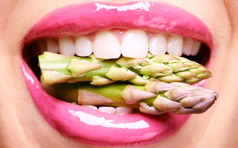 Cropped shot of a woman biting on a bunch of asparagus