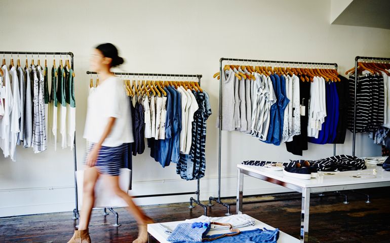 Female customer with shopping bag walking in clothing boutique
