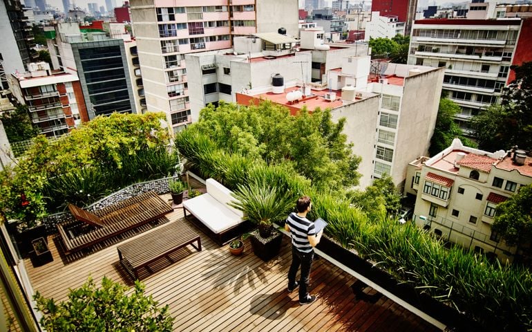 Man standing with digital tablet on rooftop garden terrace of home looking out at city skyline