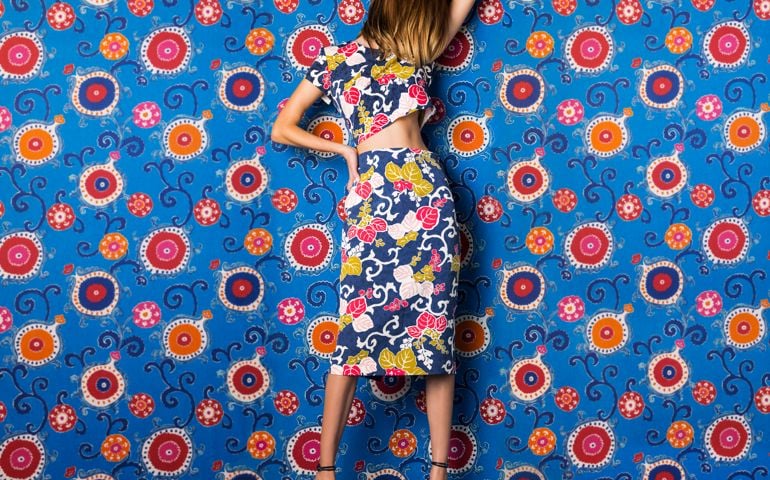 Full body photo of Beautiful young woman wearing blue floral, leaf print dress against blue, red, and orange floral print background with her hair hiding her face