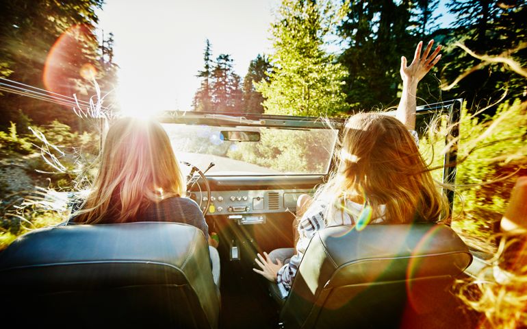 Woman riding with friends in convertible with arm outstretched in air on summer evening