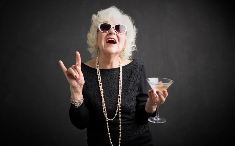 Cool grandmother with sunglasses and drink in hand showing rock sign