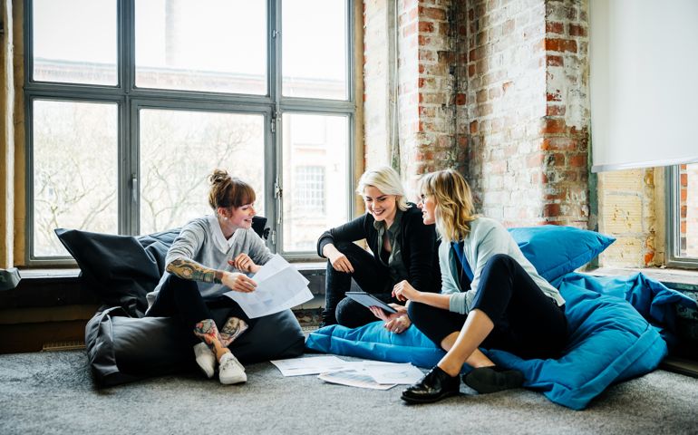 Three businesswomen sitting on large Pillows in an office and talking during an informal meeting