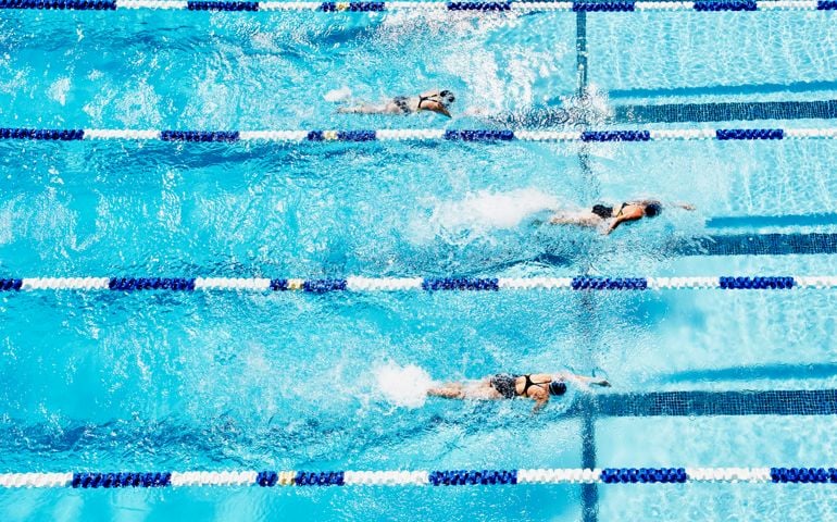 Young female competitive swimmers racing in outdoor pool overhead view