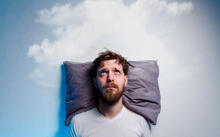 Man having problems/ insomnia, laying in bed on pillow, looking up to gray cloud over his head