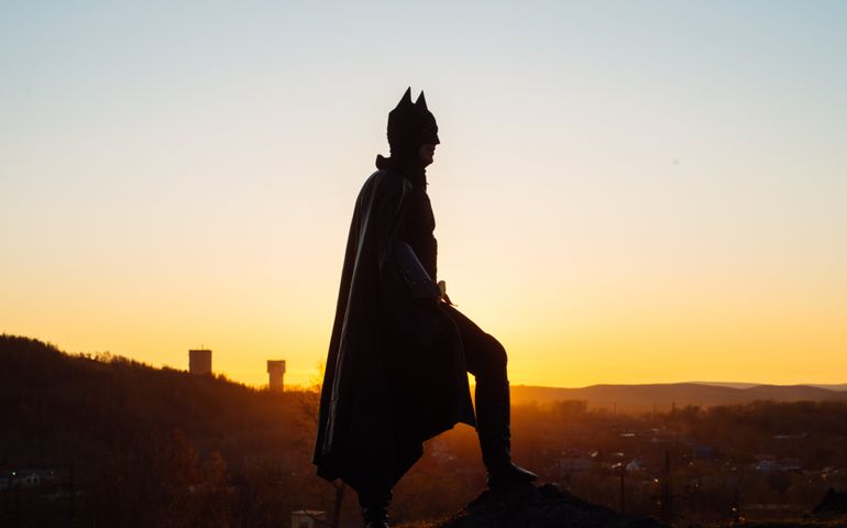 Batman cosplay-photo shoot in a suit and black cloak, at sunset over the city